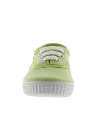 Zapatilla de lona verde con suela de goma blanca, que presenta tres ojales y cordones blancos, textura suave y diseño de punta redondeada.
