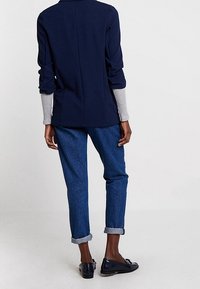 Námořnická košile s dlouhým rukávem a šedými manžetami, v kombinaci s ohrnutými modrými džíny a tmavými slip-on botami. Jednoduchý design s uvolněným střihem.