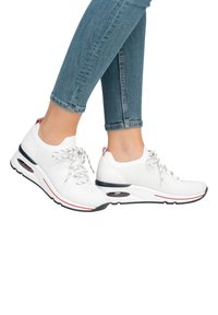 White knit sneakers with a rounded toe, lace-up front, and red and navy accents. Cushioned sole with visible air pocket, textured upper.