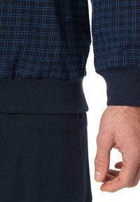 Sudadera navy con un patrón a cuadros en azul claro. Presenta puños y dobladillo acanalados. Textura de tela suave con un corte relajado.