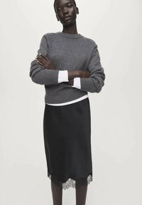 Jersey gris de punto con mangas largas, superpuesto sobre una falda negra de satén con un dobladillo de encaje. Textura lisa con un diseño de ajuste relajado.