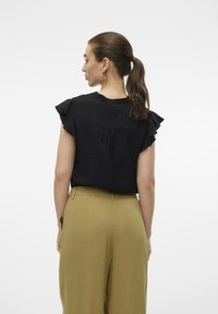 Top nero a maniche corte con dettagli arricciati, caratterizzato da un retro plissettato, abbinato a pantaloni beige a gamba larga con vita alta.