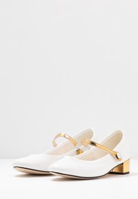 Ballerine bianche con punta appuntita, dotate di una lucida fascia d'oro e di un piccolo tacco a blocco dorato. Tessuto morbido con un accento di fascia a texture.