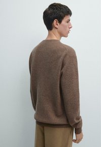 Brązowy sweter z okrągłym dekoltem, ściągaczami na mankietach i dolnym brzegu. Wykonany z dzianiny o fakturowanej strukturze, dopasowany fason, widoczny od tyłu.