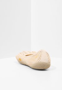 Lätt beige nät sko med rund tåform, texturerad sula och diskret logotyp. Öppen design för andningsförmåga och flexibilitet.