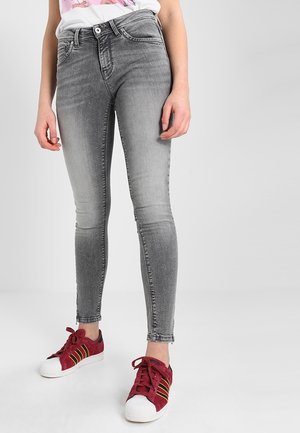Jeans skinny grises con un lavado deslavado, que cuentan con cinco bolsillos y un cierre de botón. Combinados con zapatillas rojas y una camiseta gráfica.