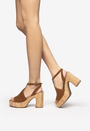Brown suede platform sandals with cork heels, featuring an open toe and ankle strap with a buckle detail.