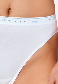 Witte katoenen slip met een lichtblauwe logo-band in de taille, versierd met kleine sterpatronen. Gladde textuur, klassieke snit.
