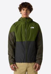 Giacca impermeabile verde e nera con zip frontale, cappuccio e due tasche laterali. Presenta un logo sul petto e blocchi di colore a contrasto.