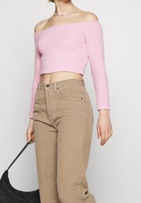 Růžový zkrácený svetr bez ramínek s texturovanou tkaninou, kombinovaný s vysokými hnědými kordovými kalhotami a černou kabelkou.