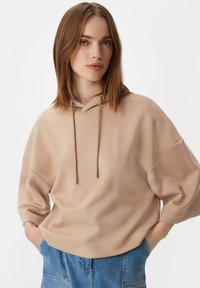 Beżowa bluza z kapturem o luźnym kroju, z oversize'owymi rękawami i srebrnymi detalami sznurków. Miękka faktura i prosty design.