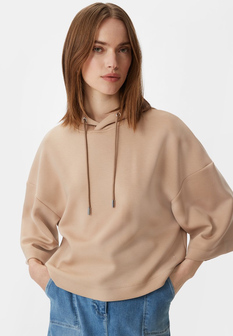 Beżowa bluza z kapturem o luźnym kroju, z oversize'owymi rękawami i srebrnymi detalami sznurków. Miękka faktura i prosty design.