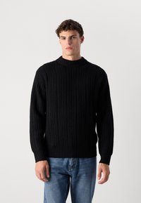 Black knitted sweater with a textured ribbed design, boat neckline, and long sleeves, paired with blue jeans.