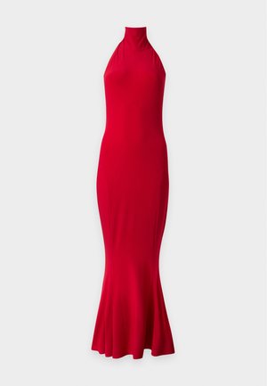 Mujer con cabello claro que lleva un vestido rojo sin mangas y de largo hasta el suelo, de pie frente a un fondo claro y liso.
