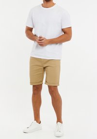 Maglietta in cotone bianca e pantaloncini beige arrotolati. Scarpe da ginnastica bianche. Design aderente con scollo tondo. Estetica semplice e pulita.