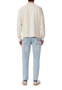 Weißer, gerippter Pullover mit langen Ärmeln und Kragen, kombiniert mit hellblauen, geraden Jeans mit Gesäßtaschen und kontrastierenden Nähten.