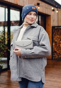 Gray wool blend shirt jacket with two chest pockets, paired with a cream knit sweater and a gray clutch. Blue ribbed beanie with polka dots.