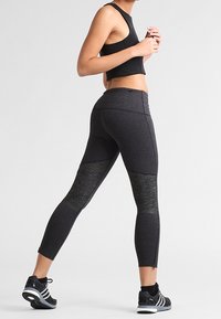 Leggings atletici neri con un design testurizzato e pannelli grigi, aderenti, con dettagli in zip alla caviglia. Abbinati a scarpe sportive nere.