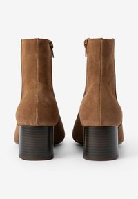 Braune Wildleder-Stiefeletten mit abgerundetem Zehenbereich und niedrigem, gestapeltem Absatz. Mit einem Reißverschluss auf der Rückseite und glatter Textur.