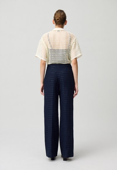 Top court en tricot ajouré crème à manches courtes associé à un pantalon large taille haute bleu marine avec des rayures texturées.