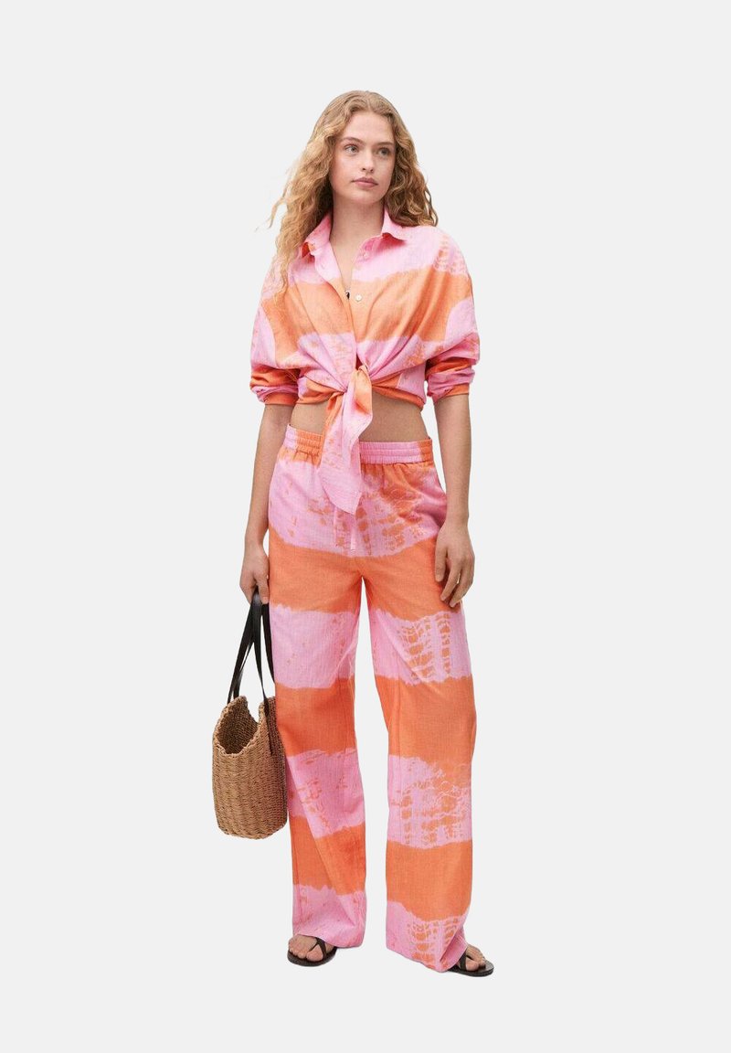 Camicia a strisce rosa e arancioni con nodo anteriore, dalla vestibilità rilassata, abbinata a pantaloni a gamba larga coordinati. Una borsa rotonda intrecciata completa il look.