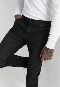 Mustat farkkuhousut, joissa tiukka istuvuus ja useita saumoja sekä ompeludetaljeja. Yhdistetty pitkähihainen valkoinen paita.