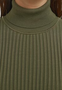 Rippstrick-Turtleneck-Oberteil in olivgrün, mit hohem Kragen und strukturiertem Stoff, der vertikale Streifen für ein strukturiertes Aussehen aufweist.