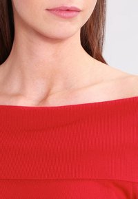 Top rosso a coste senza spalle con una texture liscia e un ampio scollo, che mette in risalto le clavicole e la zona delle spalle.