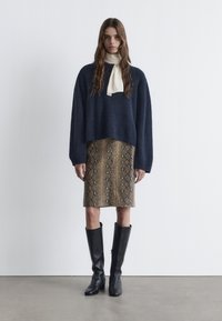 Marineblauer Strickpullover, beige Bleistiftrock mit Schlangenprint, schwarze knielange Stiefel und eine cremefarbene Krawatte; minimalistische Gestaltung und weiche Texturen.