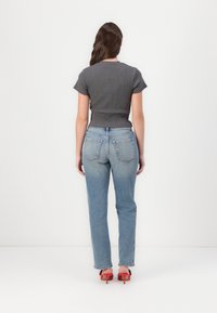 Top cinza canelado de mangas curtas combinado com jeans de perna reta azul claro. Detalhes notáveis: cintura alta e bolsos traseiros inclinados. Sapatos de salto vermelhos com tiras.