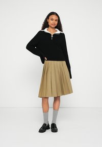 Black knit sweater with a white collar, pleated beige skirt, gray socks, and black shoes. Smooth textures and clean lines in design.