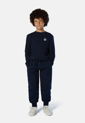 Tuta sportiva blu navy in tessuto morbido composta da una maglietta a maniche lunghe e pantaloni con vita elastica. Logo distintivo sul petto, abbinata a scarpe da ginnastica bianche.