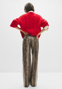 Maglione rosso oversize lavorato a maglia con motivi a treccia, abbinato a pantaloni larghi con stampa pitone metallica caratterizzati da una texture lucida.