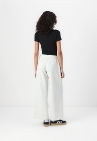 Sort kortærmet top, lys grå brede sweatpants med elastisk talje, vist bagfra, parret med sort-hvide sneakers.