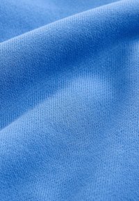Gros plan d'un tissu tricoté doux, bleu clair, avec une texture visible et des plis délicats.