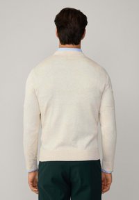 Helle beigen Pullover mit feiner Strickstruktur, Rundhalsausschnitt und gerippten Bündchen, kombiniert mit dunkelgrünen Hosen. Besitzt ein dezentes, abwechslungsreiches Farbdesign.
