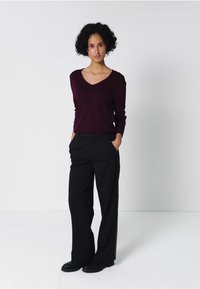 Pull en v bordeaux à manches longues, associé à un pantalon noir au fit droit avec un détail de bande latérale. Des chaussures noires complètent le look.