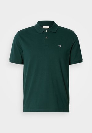 Tmavě zelené polo tričko s krátkým rukávem a dvěma knoflíky, s malým vyšitým logem na levém prsu, na bílém pozadí.