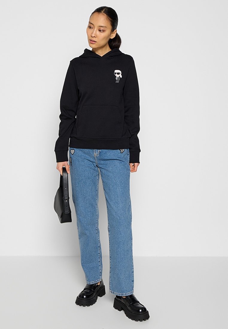 Felpa nera con cappuccio e tasca frontale, decorata con un ricamo. Abbinata a jeans blu dritti e scarpe platform nere con suola spessa.