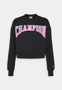 Svart kort sweatshirt i bomull, med stor rosa text "CHAMPION" över framsidan och en liten logotyp på ärmen.