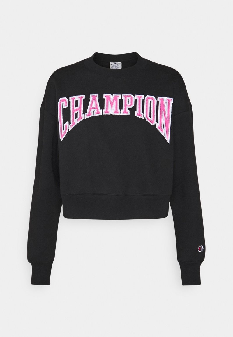 Svart kort sweatshirt i bomull, med stor rosa text "CHAMPION" över framsidan och en liten logotyp på ärmen.