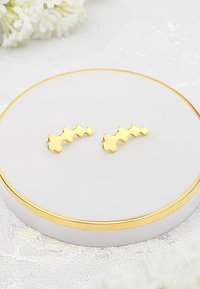 Guld-färgade örhängen med en vågig design och fyra rundade former. Visade på en cirkulär vit tallrik med en guldkant.