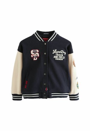 Navy blue varsity jacket with cream sleeves, white stripes, embroidered patches, and snap buttons. Features side pockets and textured fabric.