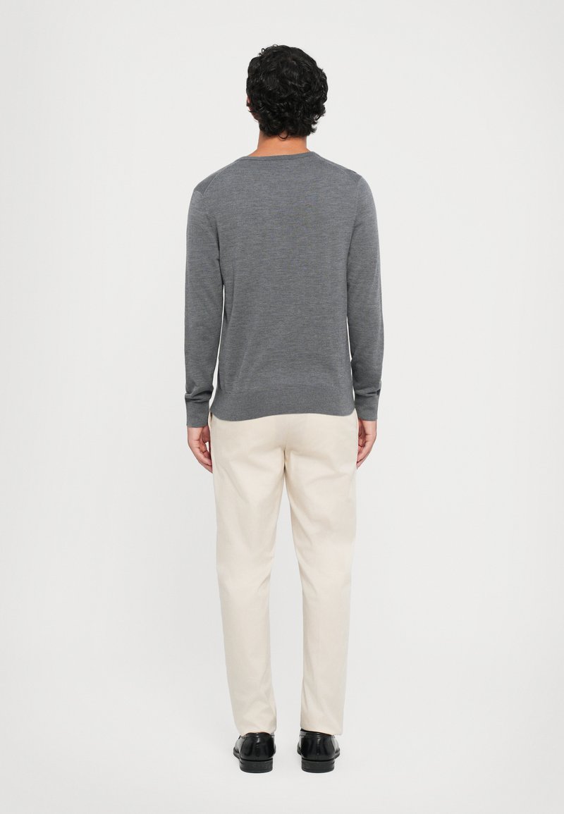 Grijze gebreide trui met lange mouwen, ronde halslijn en geribde manchetten, gecombineerd met lichtbeige broeken en zwarte schoenen, gezien vanaf de achterkant.