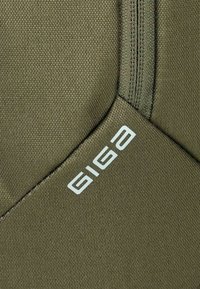 Tessuto verde oliva con superficie testurizzata, caratterizzato da un logo bianco "GIGA" sul lato e una cerniera visibile.