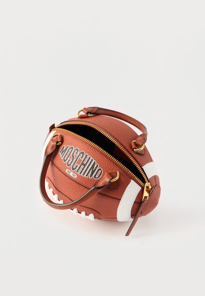 Καφέ δερμάτινη τσάντα χειρός σε σχήμα αμερικανικής ποδοσφαιρικής μπάλας με λευκά κορδόνια, χρυστό φερμουάρ, χερούλια και το λογότυπο "Moschino" στο πλάι.