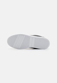 Black sneaker sole with a white outsole. Textured rubber for grip, featuring parallel grooves and branding near the heel.