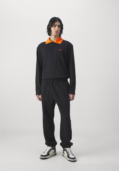 Sort langærmet polo med en orange krave og broderet logo, parret med sorte trækbåndsunderdel og høj-top sneakers med cremefarvede accenter.