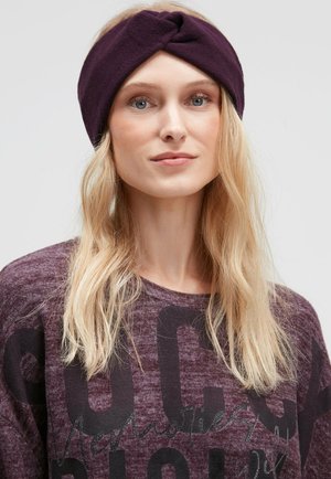 Purple fleece headband with a twisted design. Worn with a matching purple sweater featuring large black letters and a subtle texture.