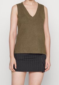 Olivgrön ärmlös topp med V-ringning, ribbad textur och avslappnad passform, matchad med en svart rutig kjol.